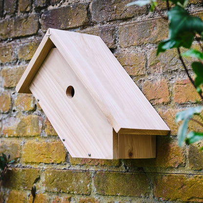 Wooden birdhouse attached to a brick wall with a brand label.