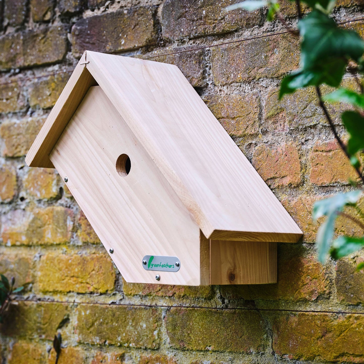 Wooden birdhouse attached to a brick wall with a brand label.