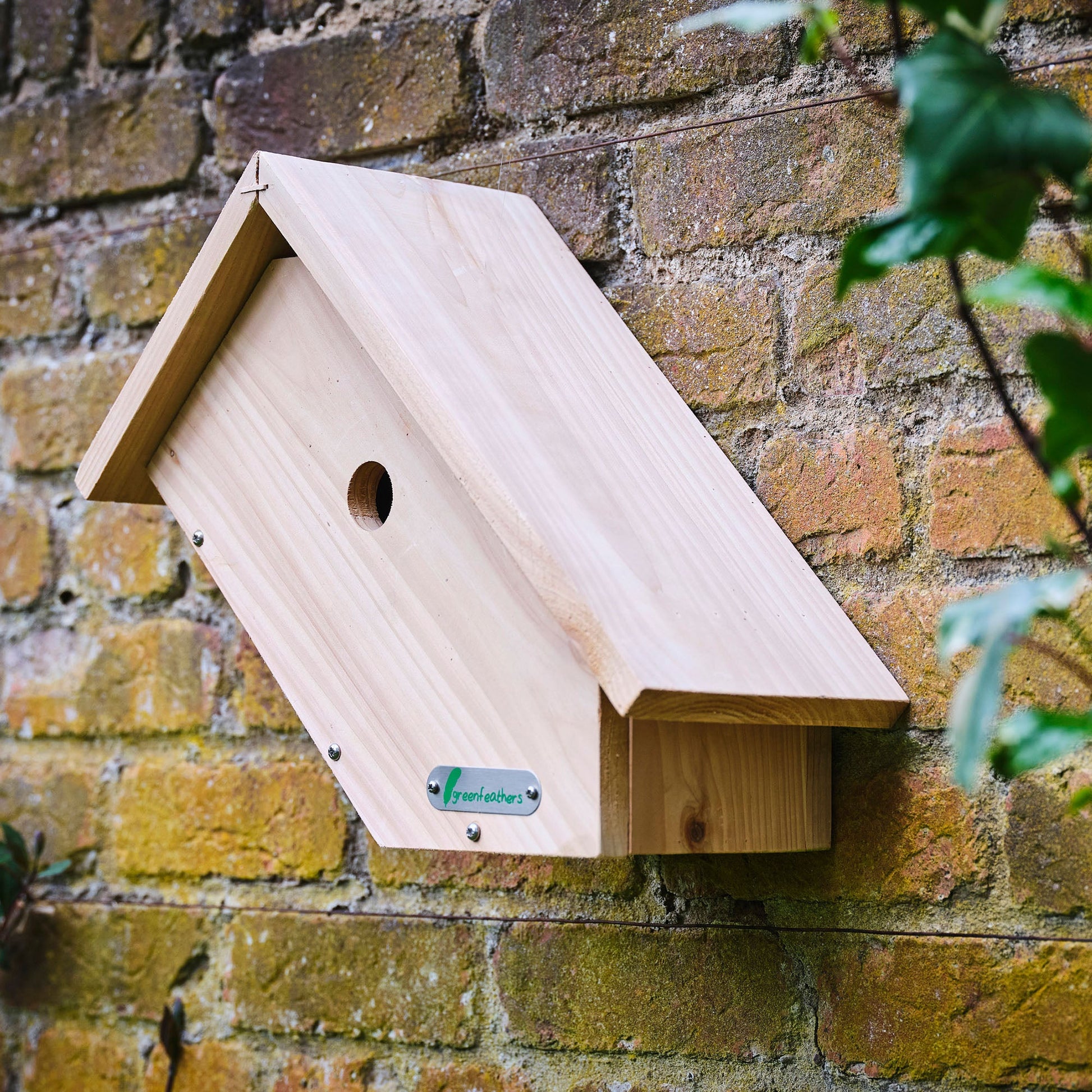 Wooden birdhouse attached to a brick wall with a brand label.