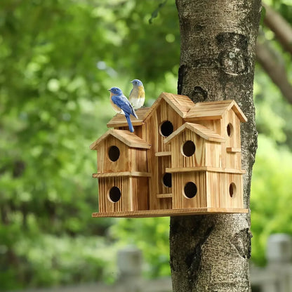 Multi-gabled wooden birdhouse on a tree with two bluebirds perched on the roof