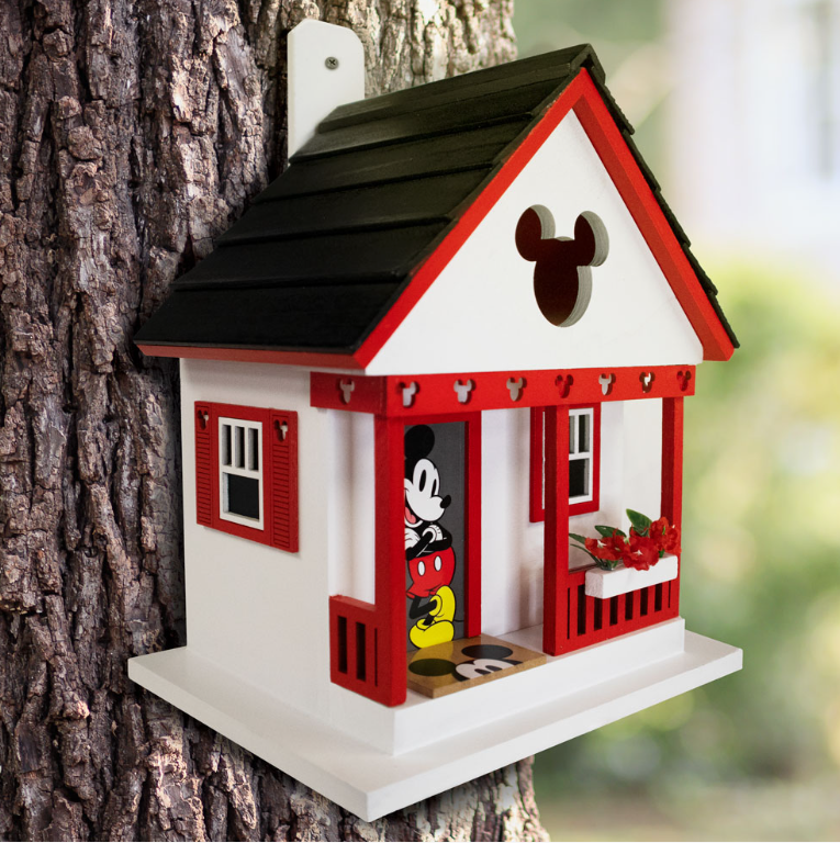 Disney Mickey Mouse Cottage Wooden Birdhouse mounted on a tree trunk by its wooden mounting paddle, with Mickey on the porch