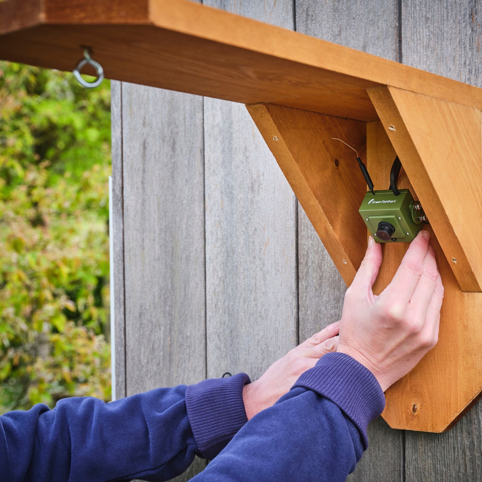 Person installing a green electronic device on a wooden shelf outdoors.