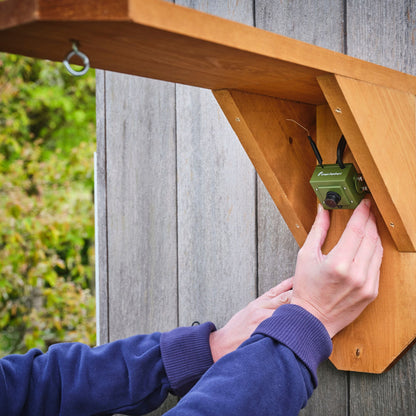 Person installing a green electronic device on a wooden shelf outdoors.
